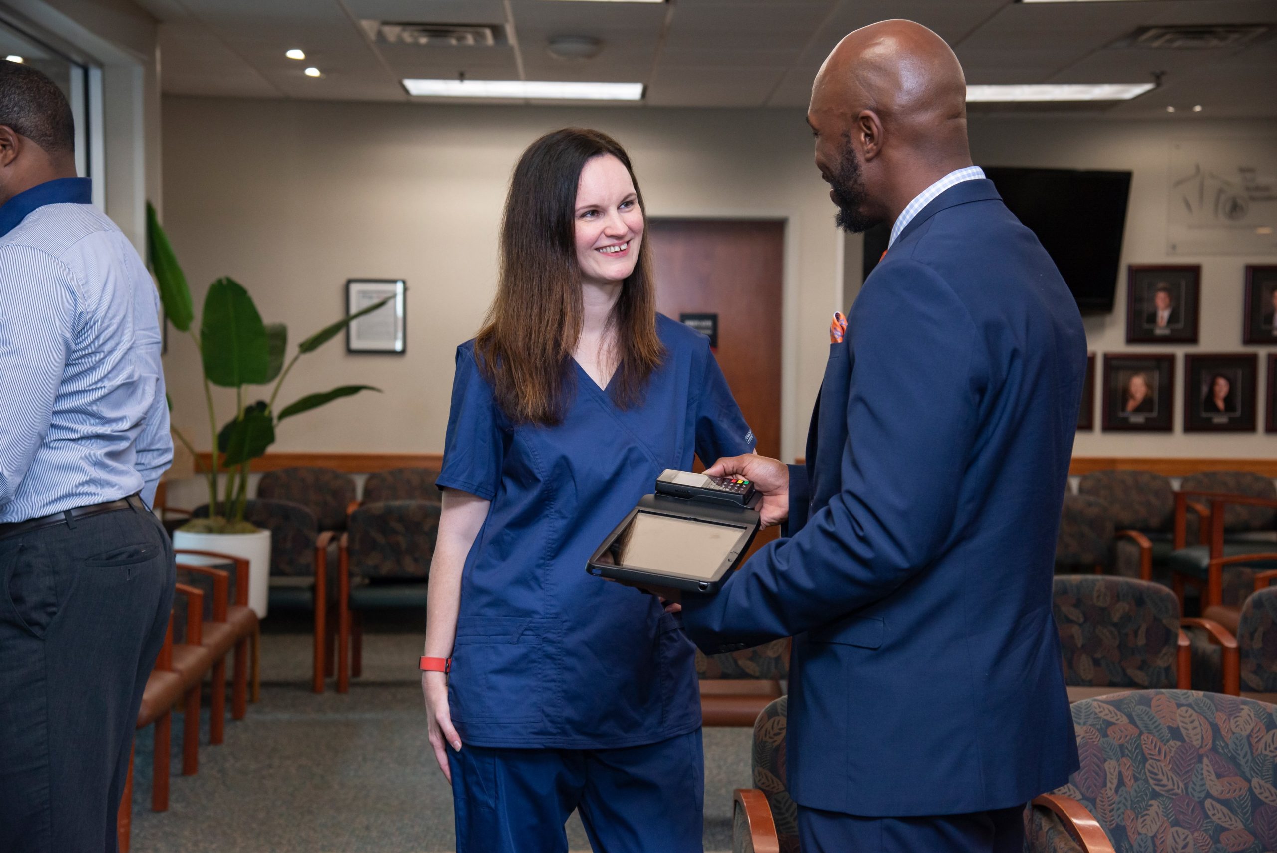 A front-office staff helps a patient check-in using a tablet intake solution.