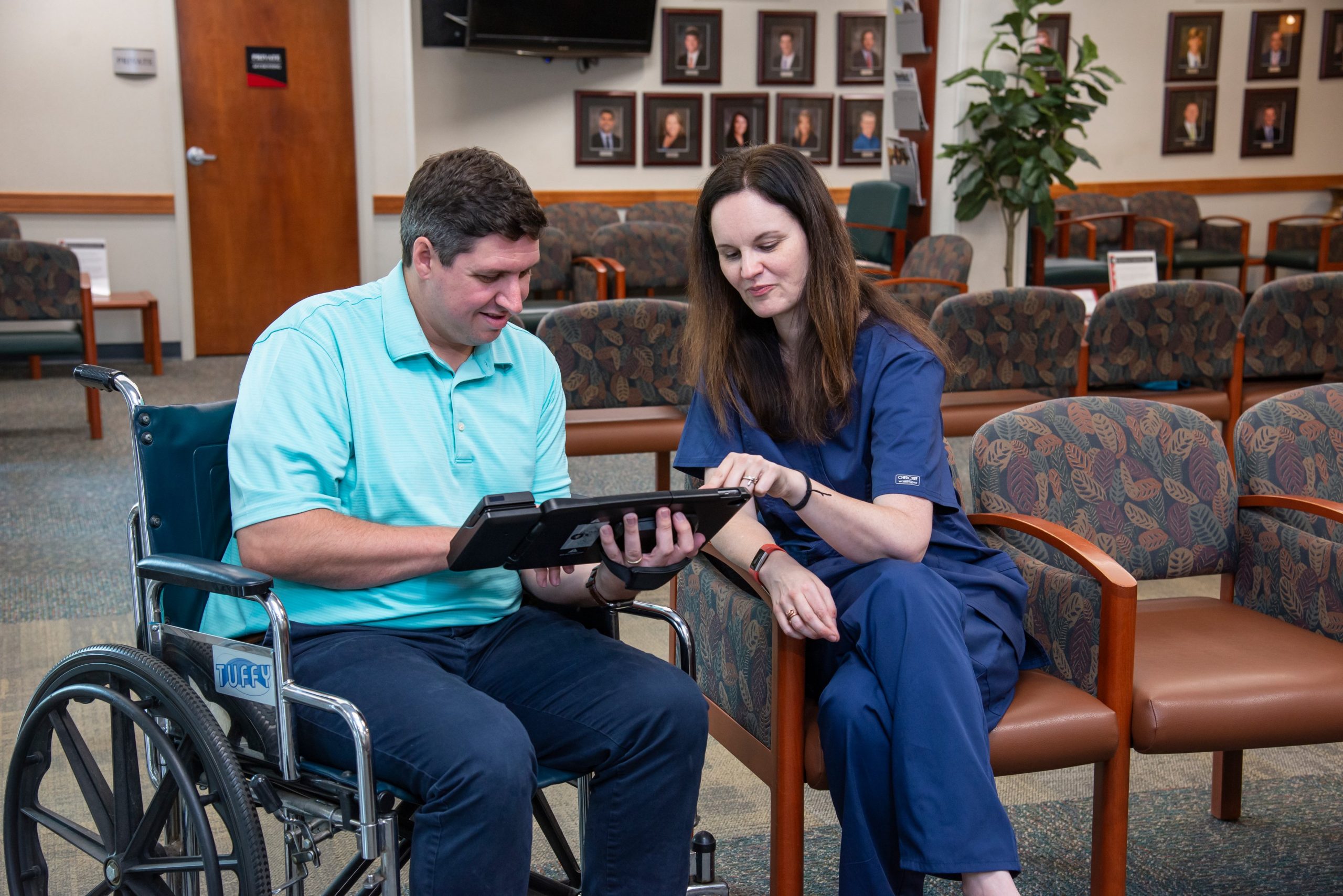 Woman assisting man in wheelchair with checking in to medical appointment using the Clearwave Connect tablet