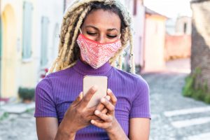 woman using cell phone outside while wearing protective face mask