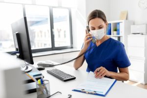 A woman in medical clothing wearing a face mask and answering a phone